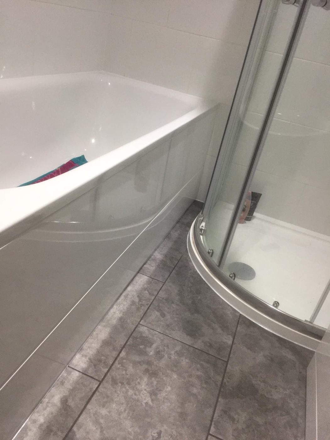 Bathroom with large grey tiles, bath and curved shower screen